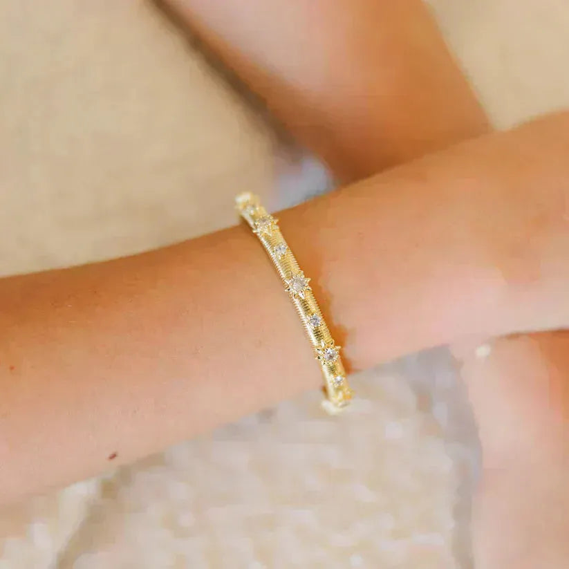 Gold Taylor Shaye bangle bracelet with small clear star-shaped studs, worn on a wrist.