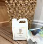 Thomas Blonde Laundry Co. 32oz scented laundry detergent in white jug with gold label, next to a wicker basket and colorful