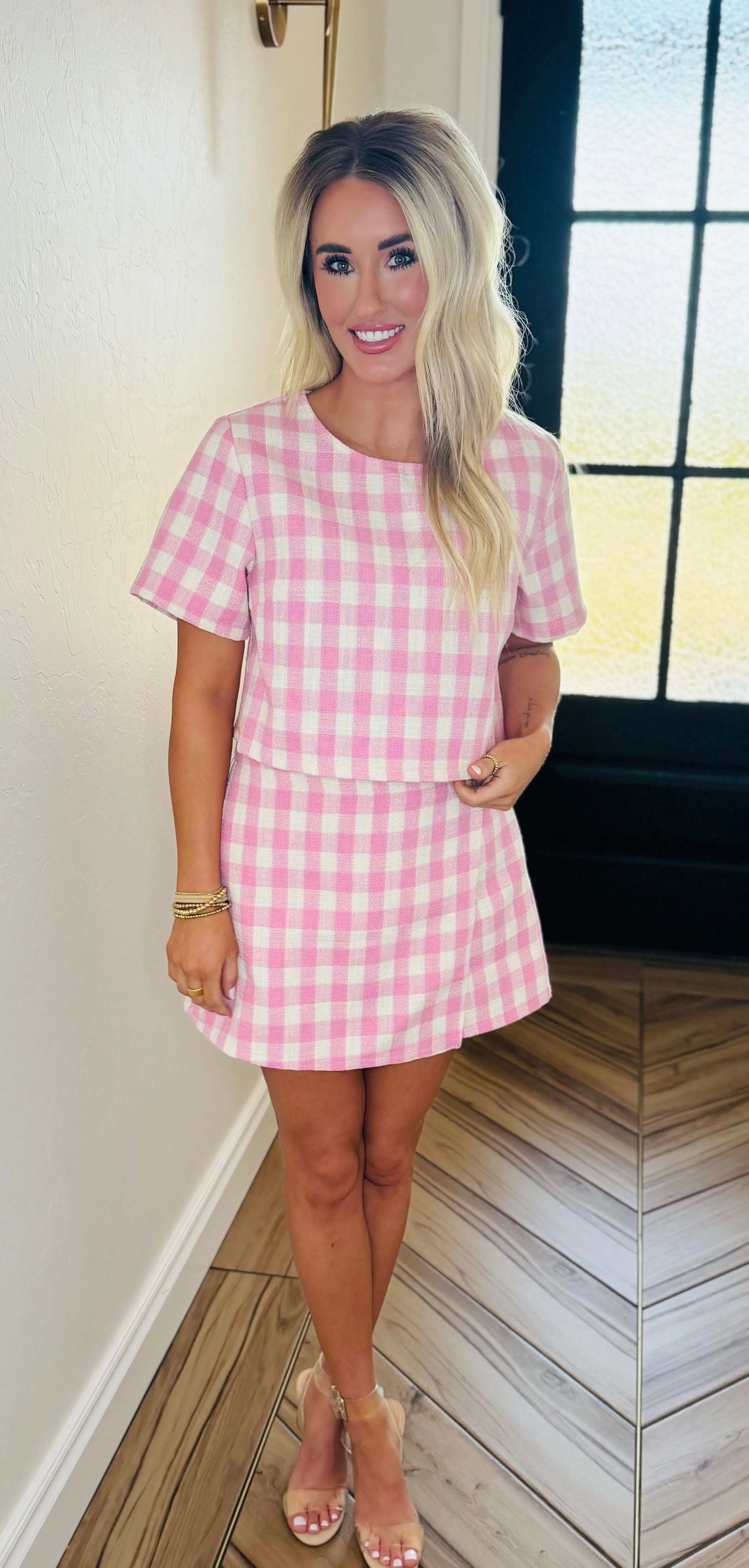 Pink gingham tweed skort set with short sleeves and a matching skirt. Woman wearing gold bracelets and ring.