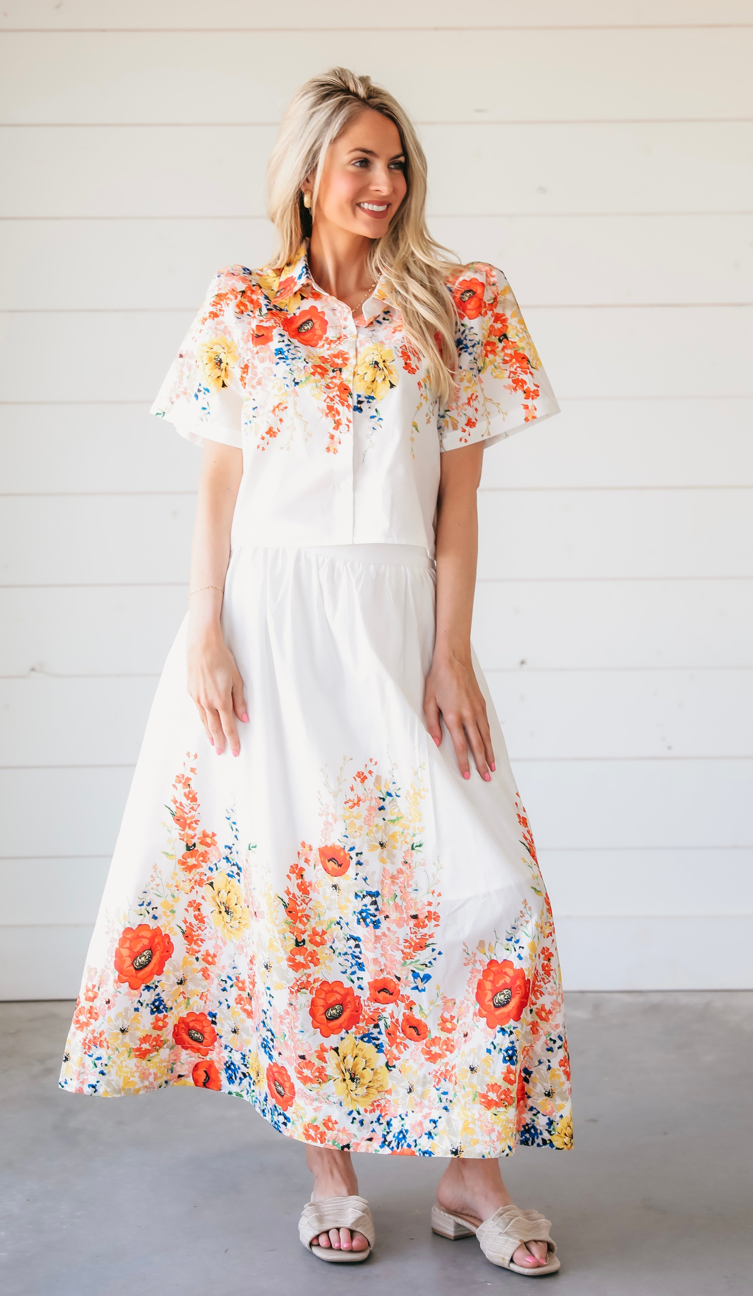 White floral two-piece maxi skirt set. Short-sleeve collared top and flowy maxi skirt with vibrant floral print of red