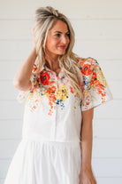 Woman wearing a white two-piece maxi skirt set. The top features a vibrant floral print with red, orange, and yellow